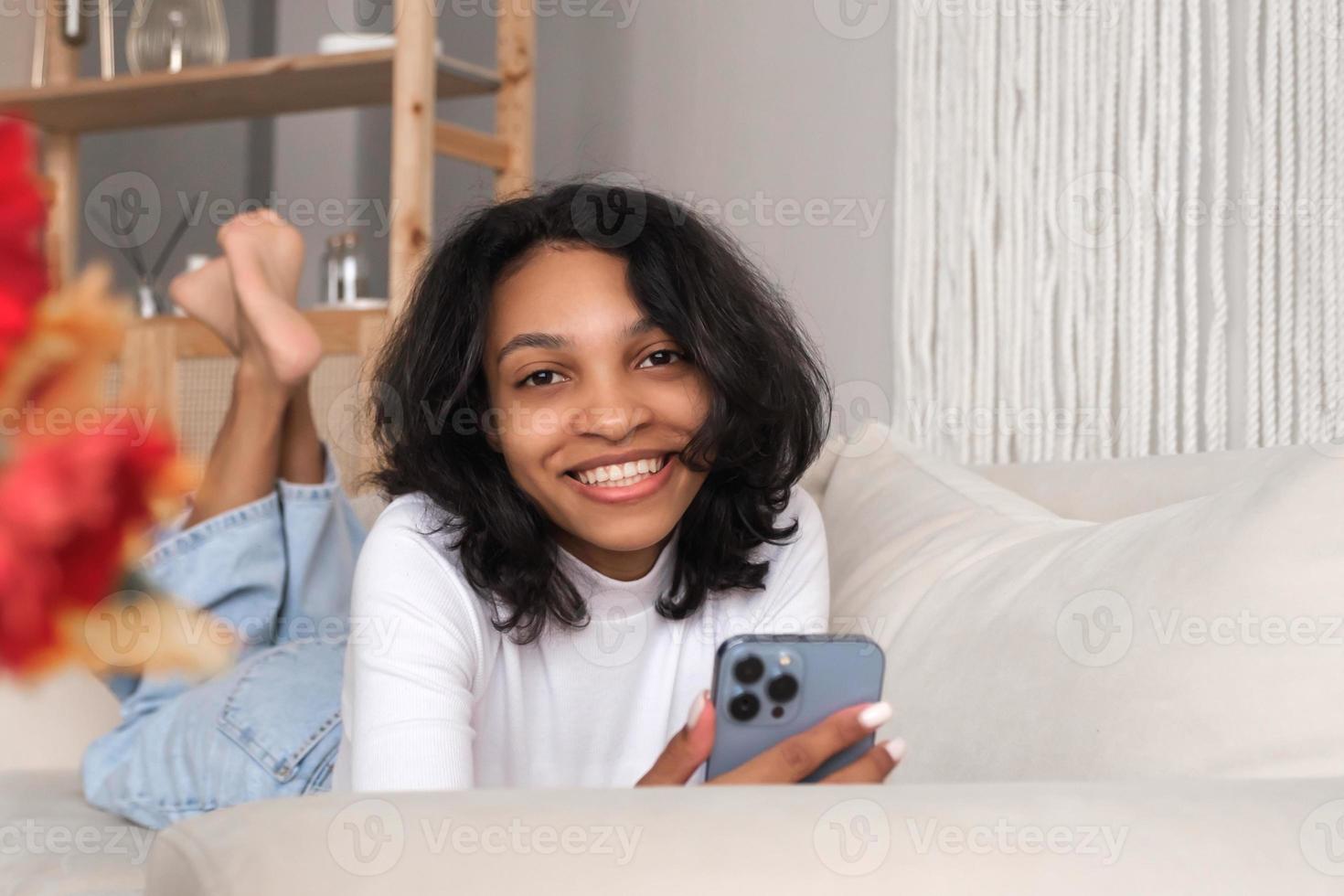 tondu de face vue portrait de content africain américain femme en utilisant téléphone intelligent fot SMS, livraison, en ligne sortir ensemble photo