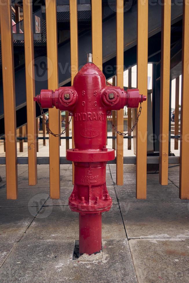 une rouge Feu bouche d'incendie avec deux bras sur tous les deux côtés. d'or clôture Contexte. supporter tuyau bouche d'incendie Extérieur. photo