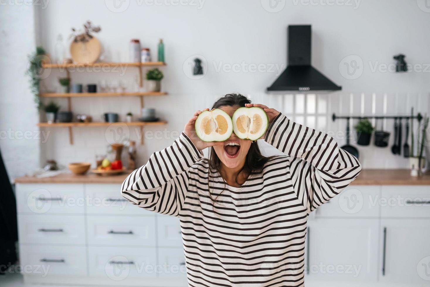 une femme tient des fruits coupés au niveau des yeux au lieu de lunettes photo
