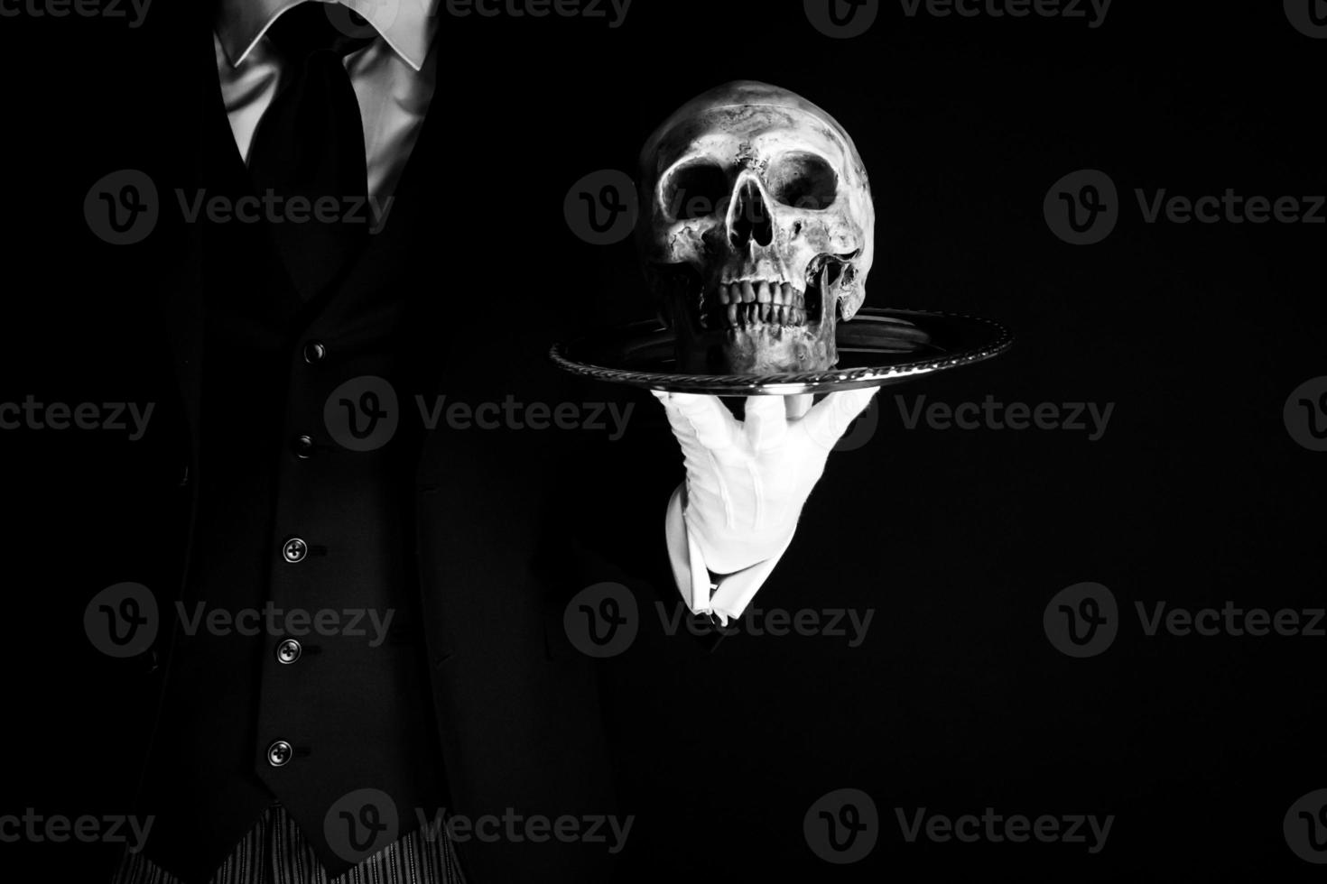 portrait de majordome ou serveur dans foncé costume et blanc gants en portant crâne sur plateau. concept de horreur et Halloween. inquiétant et affreux décès. photo