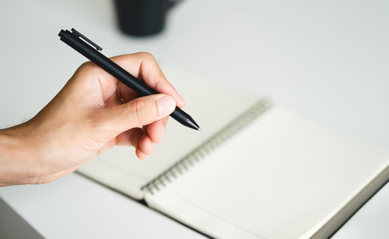 la gauche remis homme en portant une stylo et l'écriture dans une carnet sur le table photo