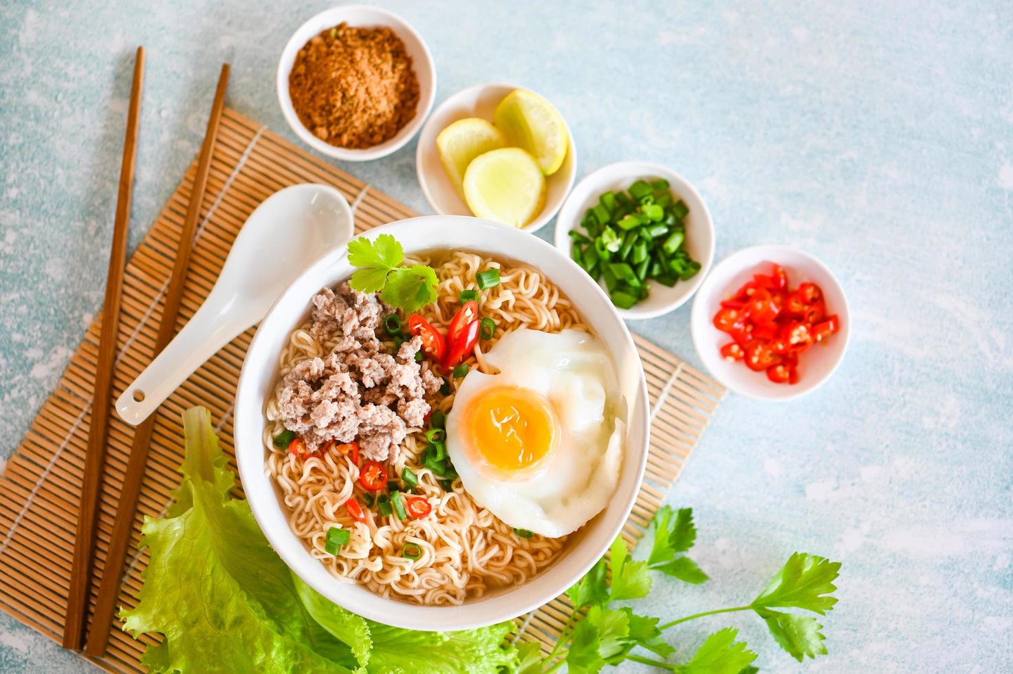 bol de nouilles avec œuf à la coque porc haché légume oignon de printemps citron vert laitue céleri et piment sur table nourriture, nouilles instantanées cuisine savoureuse manger avec un bol de soupe de nouilles photo