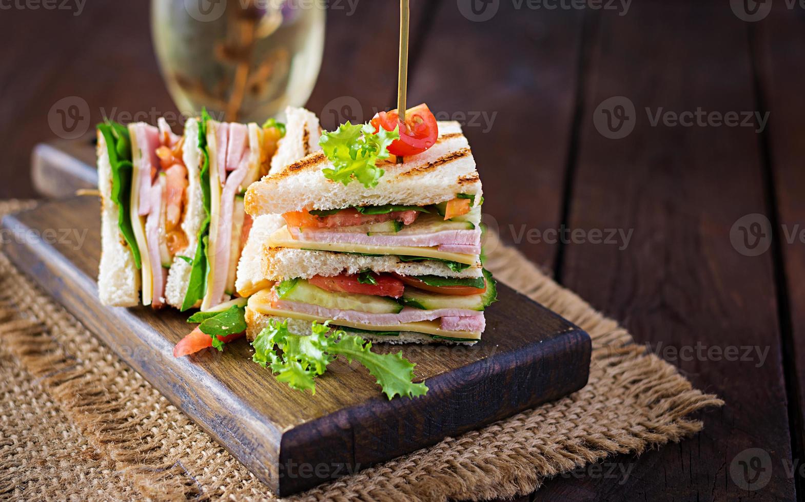 club sandwich avec jambon, tomate, concombre, fromage, et Roquette sur en bois Contexte. photo