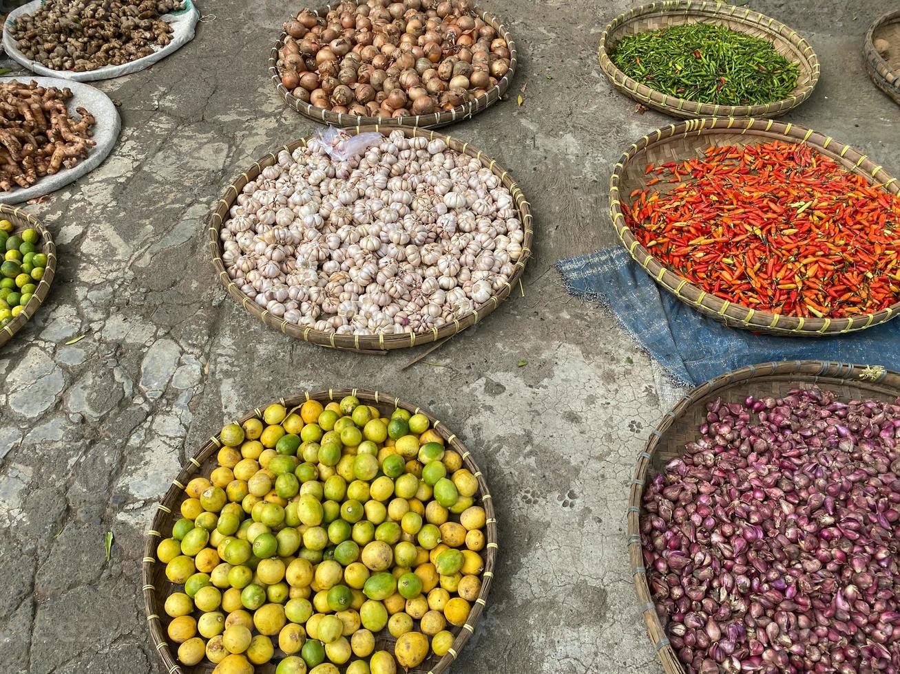 divers des légumes tomates, Chili, rouge oignon, maïs, carotte, chaux, Ail étant vendu à asiatique traditionnel marché. coloré des légumes sur rond bambou plateau à traditionnel marché sol photo