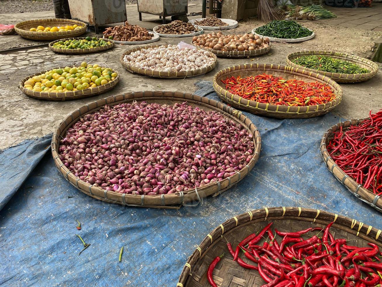 divers des légumes tomates, Chili, rouge oignon, maïs, carotte, chaux, Ail étant vendu à asiatique traditionnel marché. coloré des légumes sur rond bambou plateau à traditionnel marché sol photo