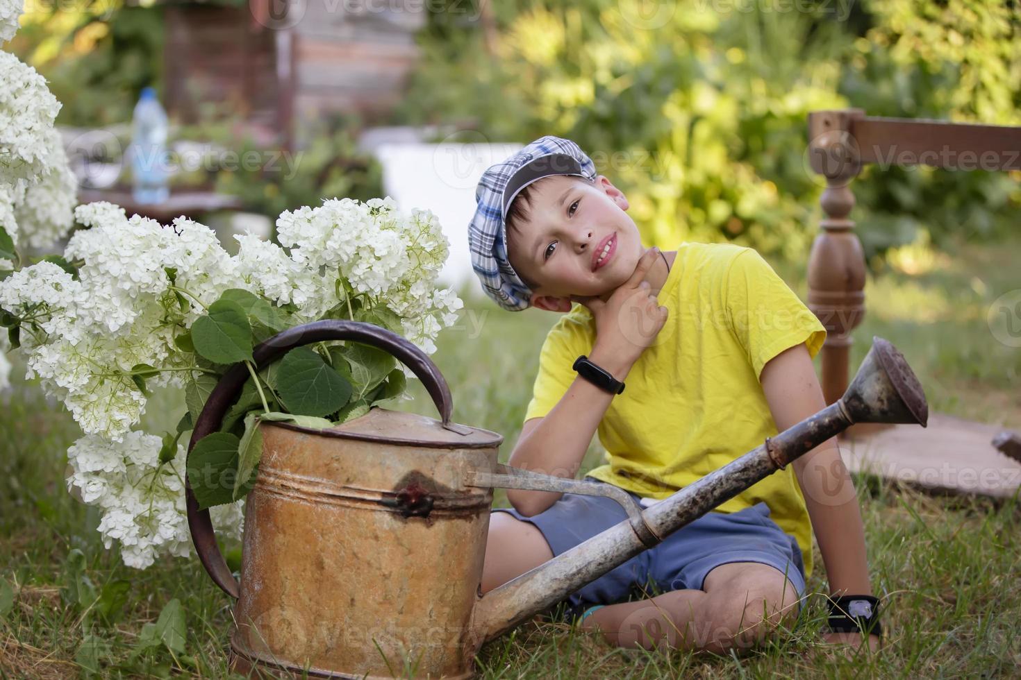 l'enfant travaille dans le jardin. garçon avec un arrosoir vintage et un bouquet de fleurs. photo