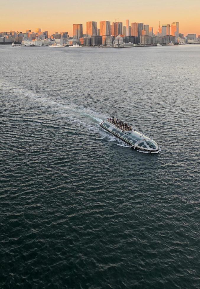 Tokyo, Japon - décembre 27, 2022 - une traversier bateau sur tokyo baie avec le ville horizon dans le arrière-plan, illuminé par le réglage Soleil. photo