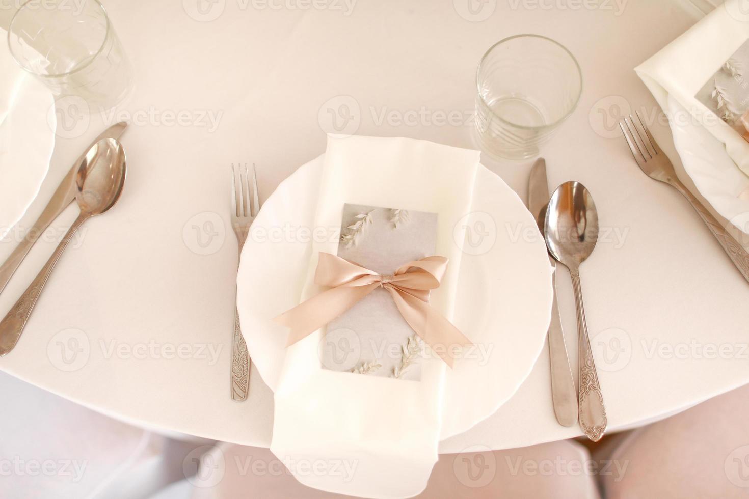 mariage table réglage avec blanc plaque, des lunettes et argent coutellerie. maquette Vide avec rose ruban sur assiette photo
