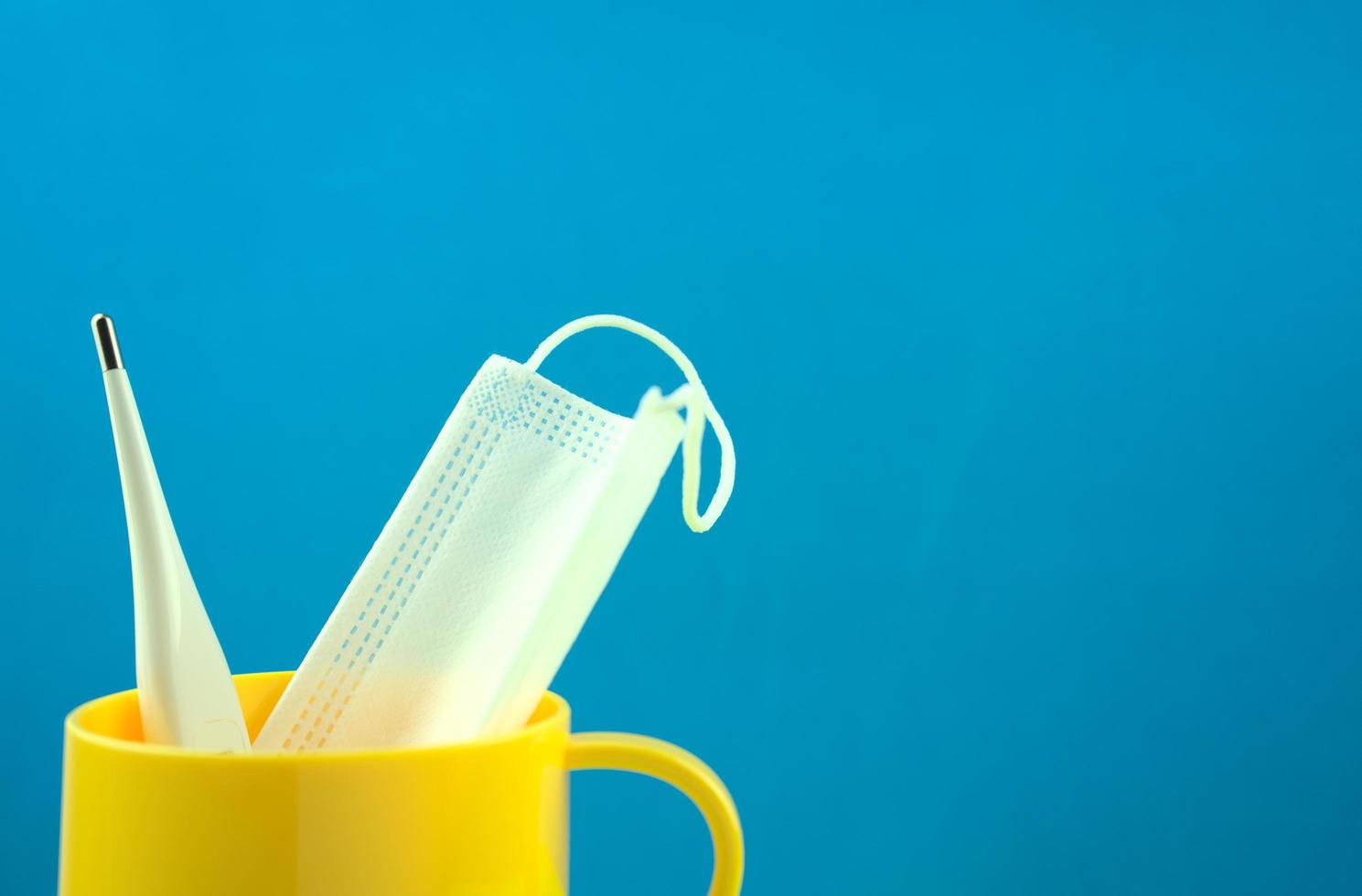 masque médical et thermomètre de température à affichage numérique dans une tasse jaune photo