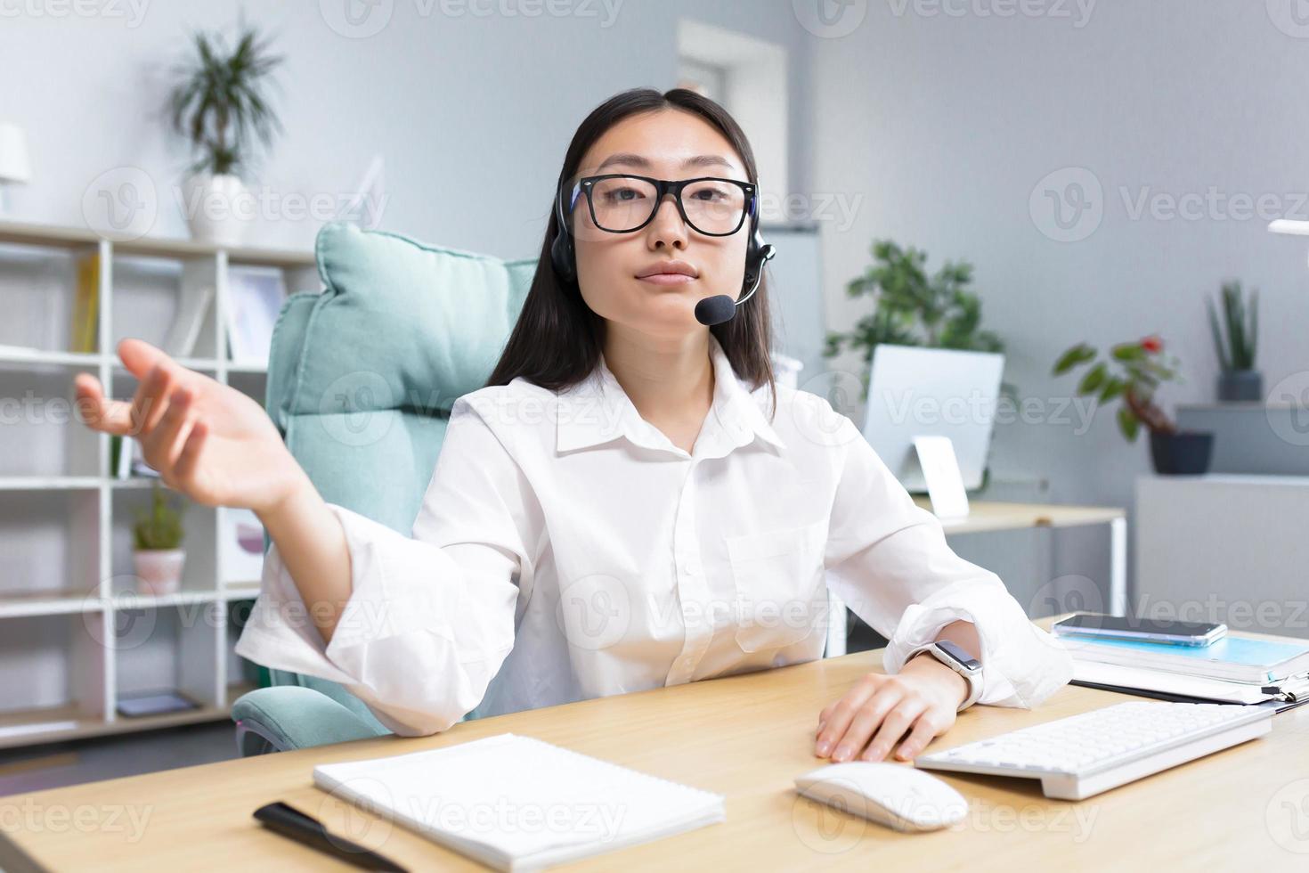 asiatique femme dans écouteurs avec une microphone, séance dans le Bureau conduite un en ligne séminaire en ligne photo