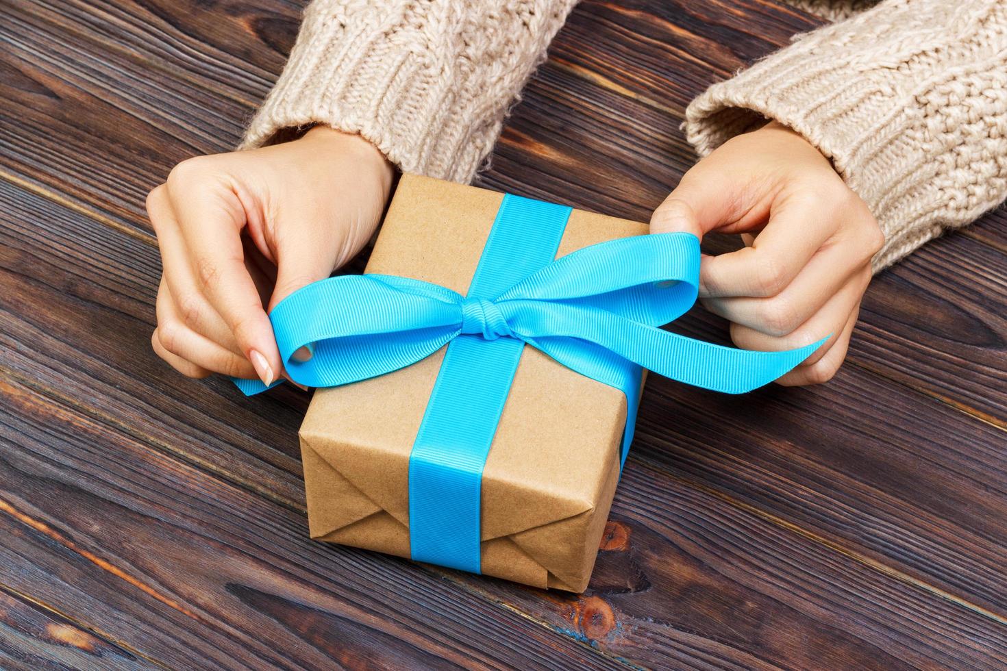 les mains de la femme donnent la saint-valentin enveloppé ou un autre cadeau de vacances fait à la main dans du papier avec un ruban bleu. boîte cadeau, décoration de cadeau sur table en bois blanc, vue de dessus avec espace de copie photo