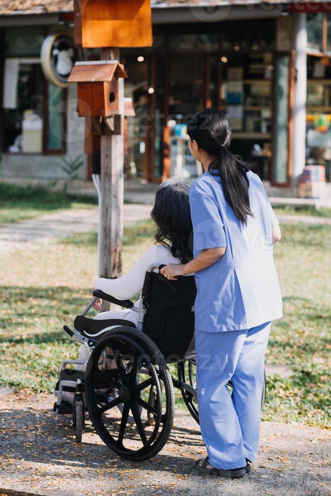 asiatique Jeune soignant infirmière soutien Sénior plus âgée Masculin en marchant en plein air. spécialiste fille médecin Aidez-moi et prendre se soucier de personnes âgées mature homme patient Faire physique thérapie dans Publique parc à allaitement maison. photo