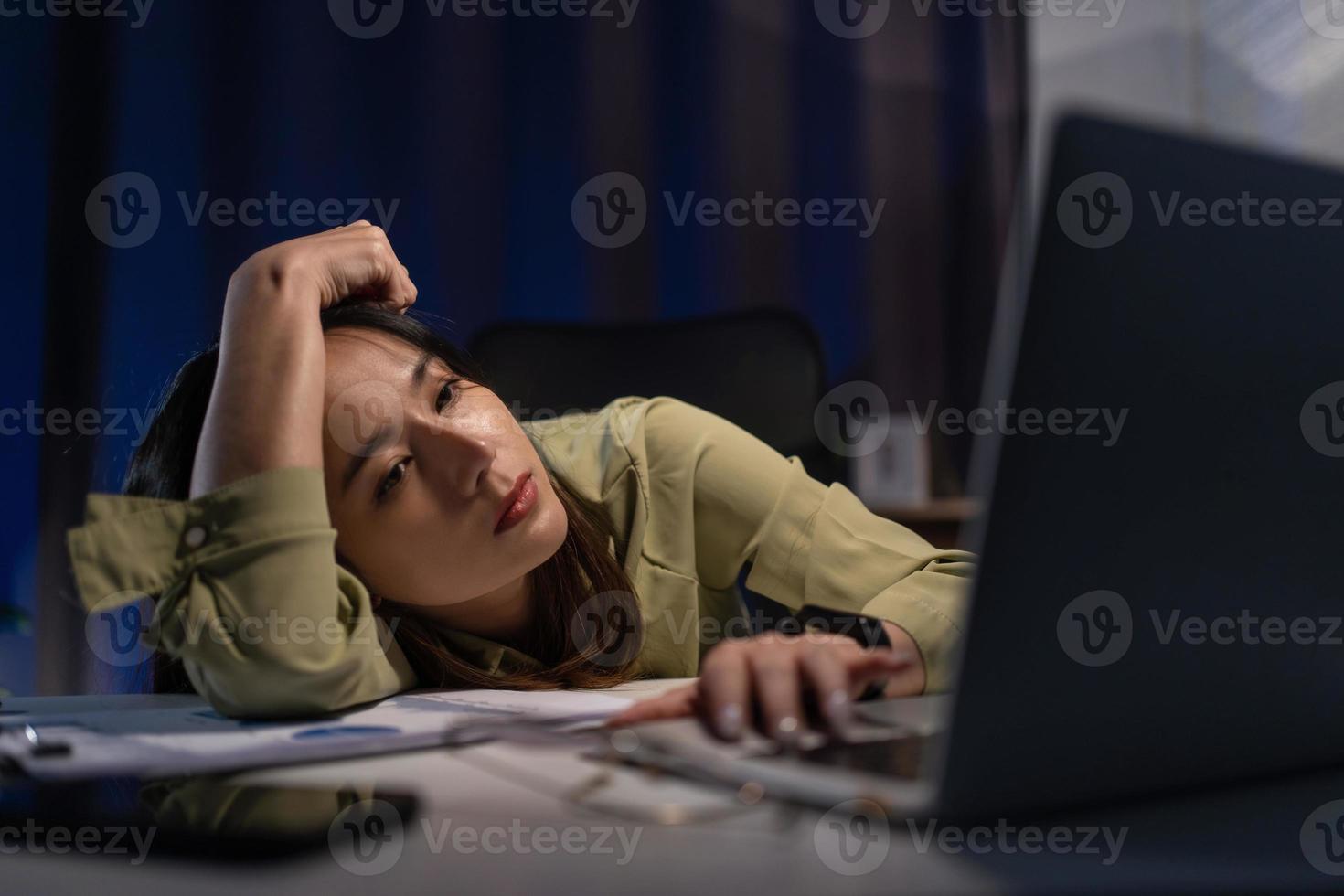 somnolent épuisé asiatique Jeune femme d'affaires travail à Bureau bureau avec sa ordinateur portable, sa yeux sont fermeture. heures supplémentaires travail concept photo