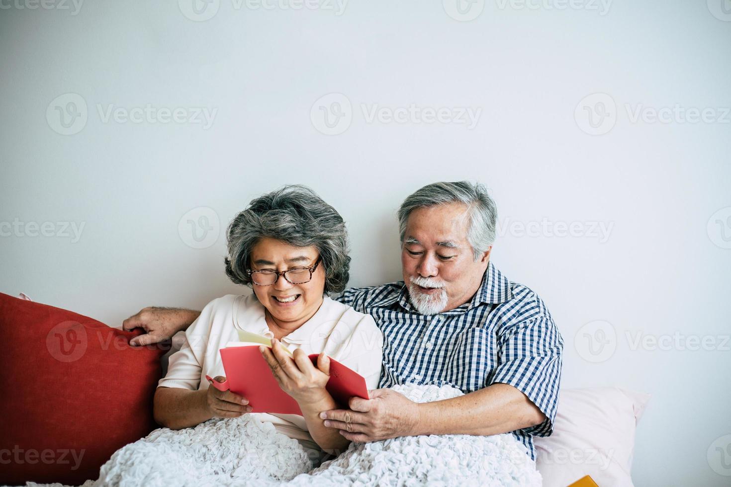 couple de personnes âgées allongé sur le lit et lisant un livre photo