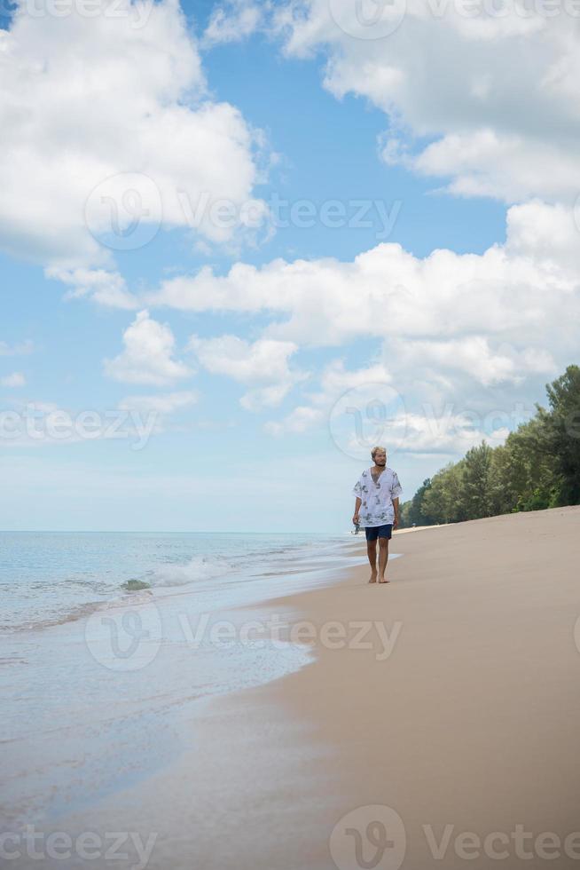 homme hipster marche sur le fond de la belle plage avec des nuages blancs et beau ciel photo