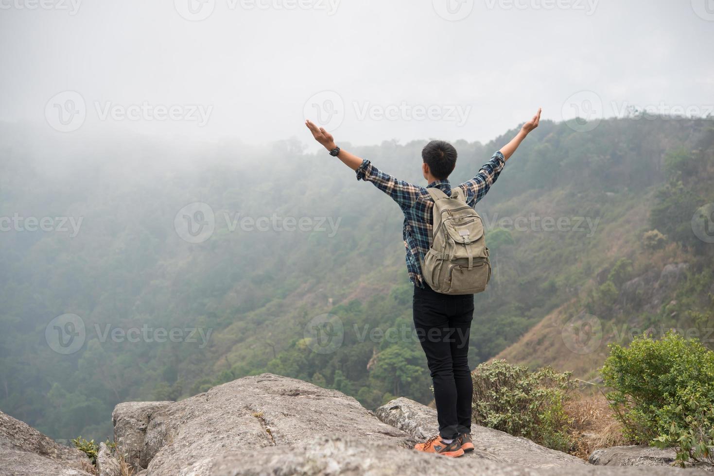 Randonneur avec sac à dos debout au sommet d'une montagne avec les mains levées photo