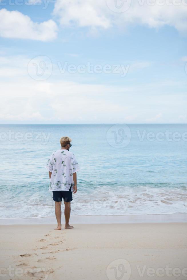 homme hipster marche sur le fond de la belle plage avec des nuages blancs et beau ciel photo