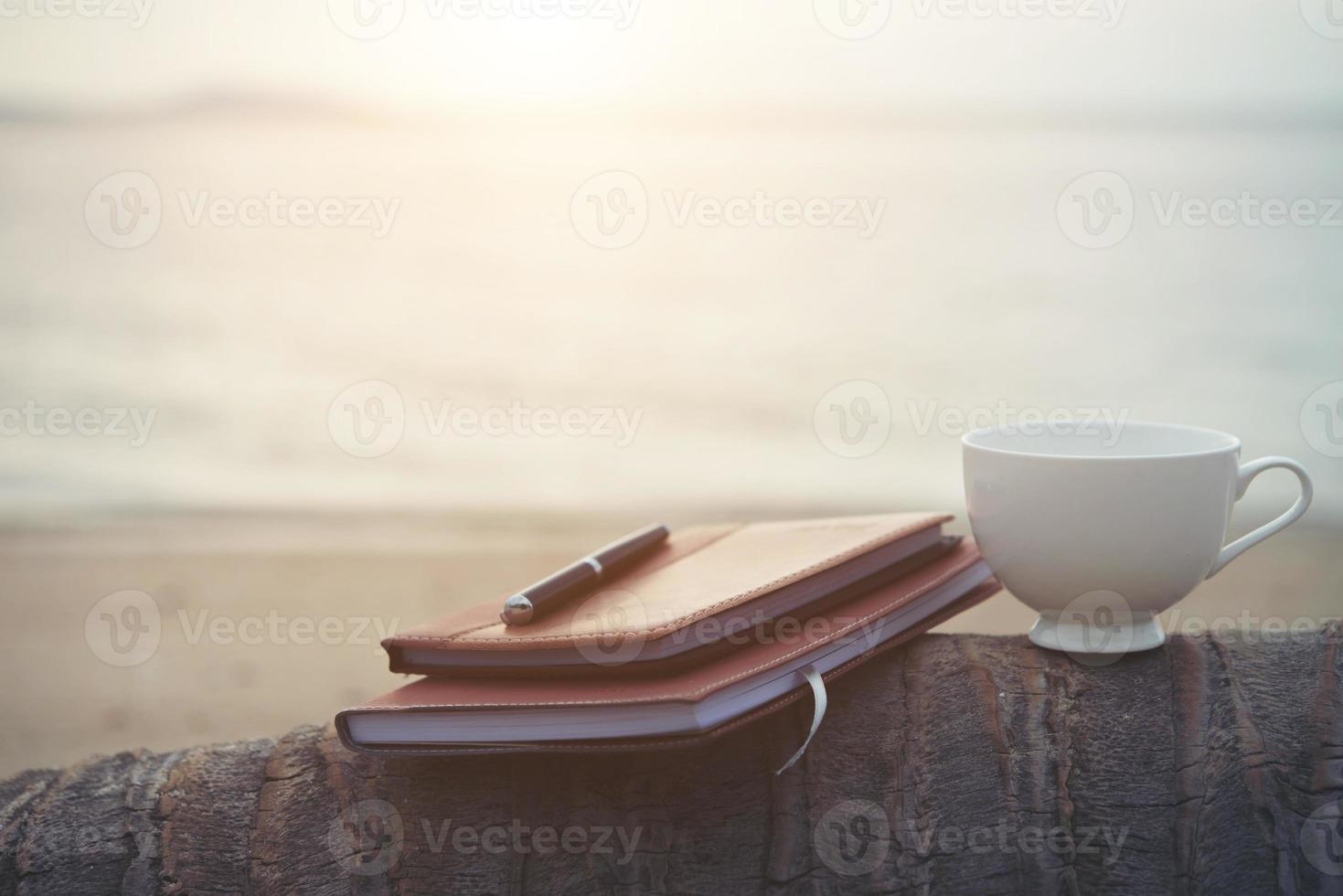 cahiers, livres, stylo et une tasse de café sur la plage photo