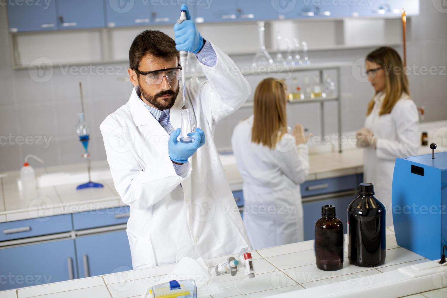 Jeune chercheur en vêtements de travail de protection debout dans le laboratoire et flacon d'analyse avec liquide photo