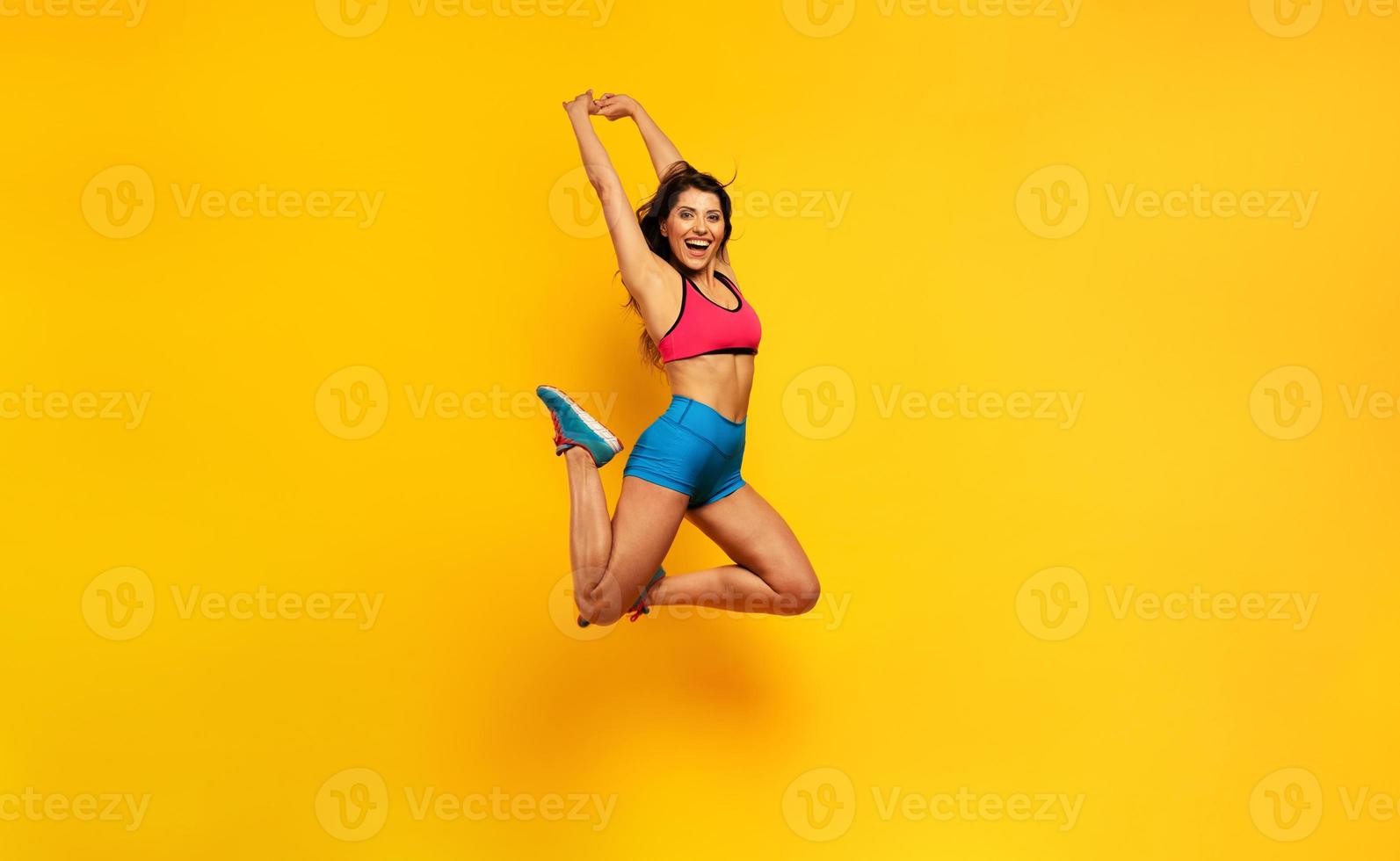 sport femme sauts sur une Jaune Contexte. content et joyeux expression. photo