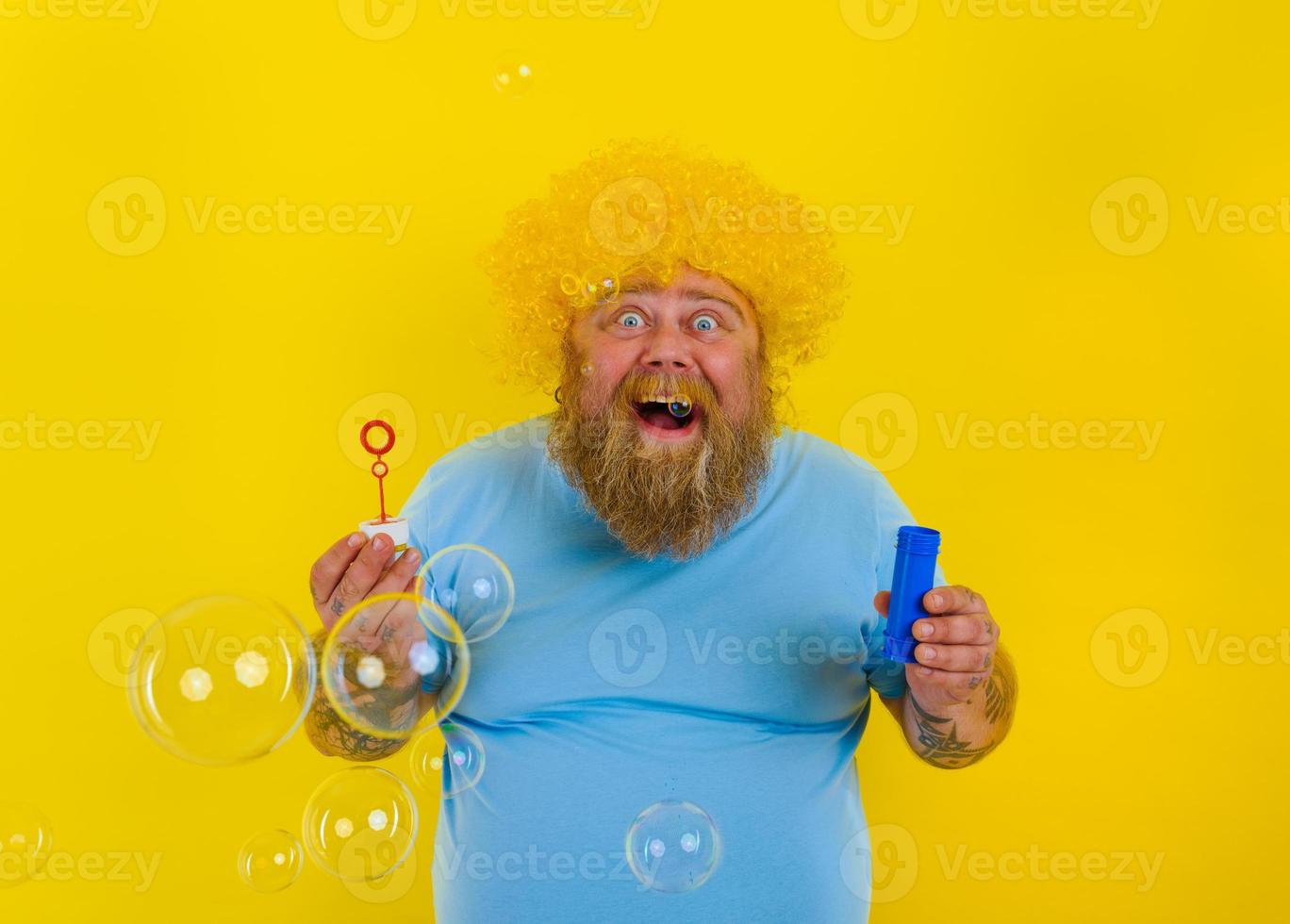 étonné homme avec Jaune perruque dans tête jouer avec bulles savon photo