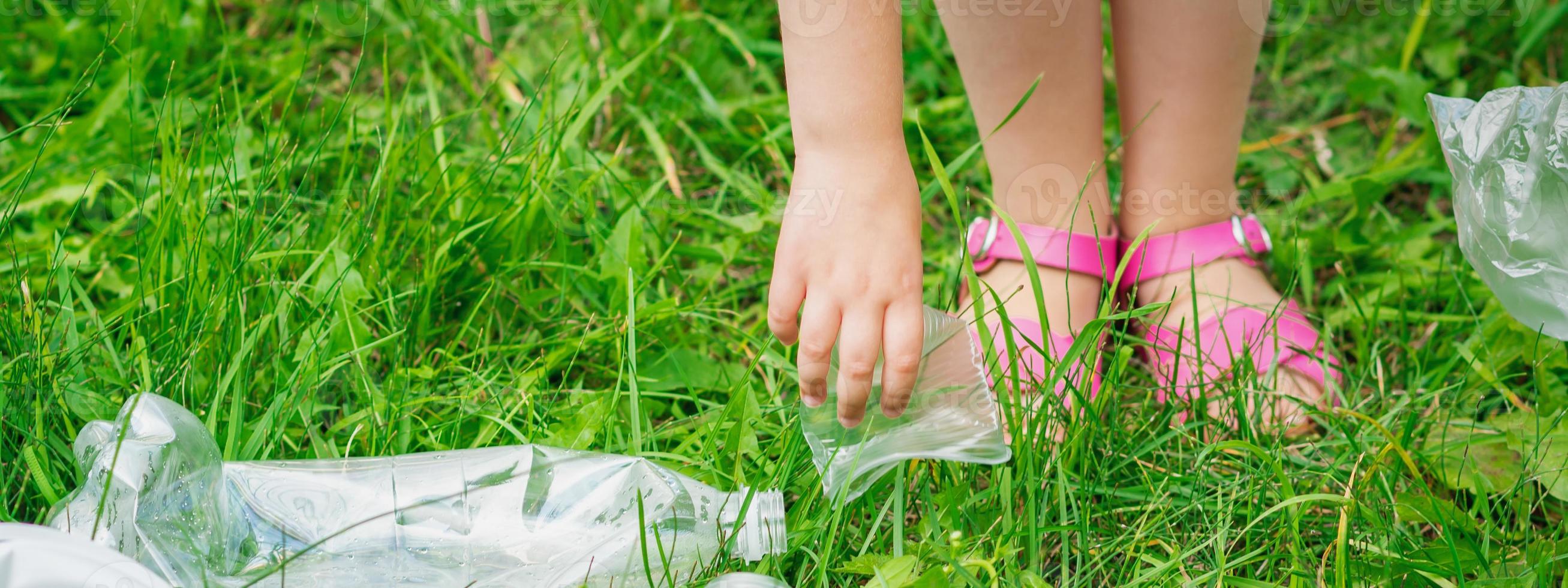 la main de l'enfant nettoie l'herbe verte des déchets en plastique photo