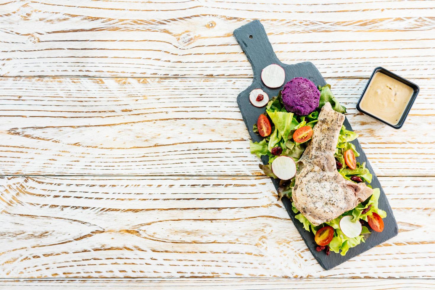 Steak de viande de côtelette de porc barbecue grillé sur plaque noire avec des légumes photo