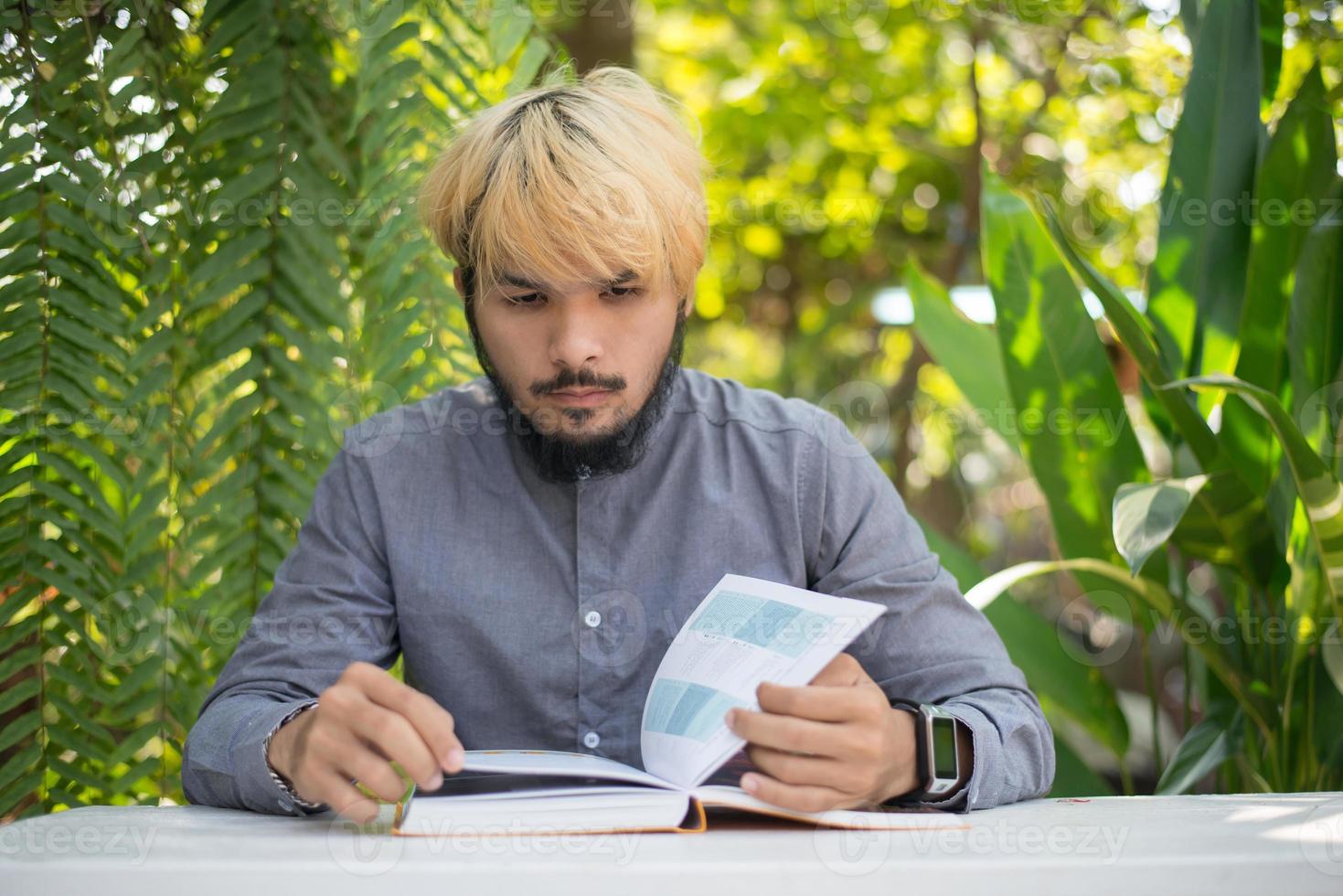 Jeune homme barbu hipster lisant des livres dans le jardin avec la nature photo