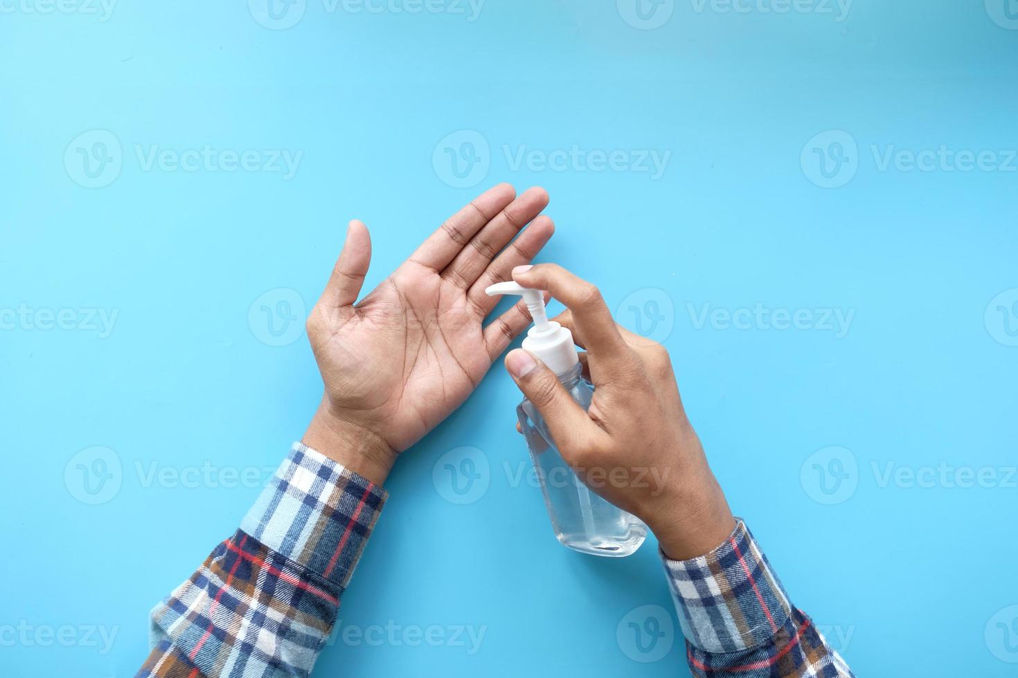 Homme appliquant un gel désinfectant pour les mains sur fond bleu photo