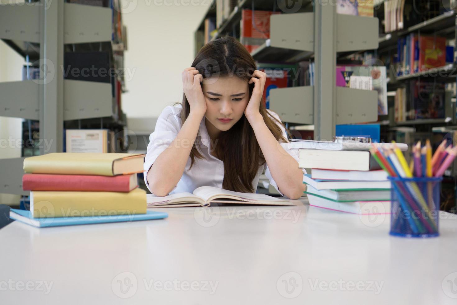 Portrait d'étudiant touchant la tête en lisant un livre dans la bibliothèque du collège photo