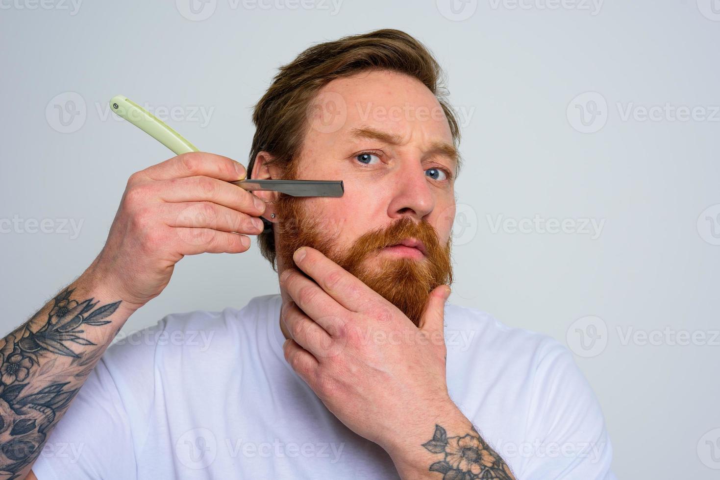 sérieux homme avec lame est concentré sur Coupe le sien barbe photo