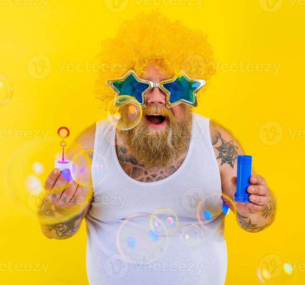 étonné homme avec Jaune perruque dans tête jouer avec bulles savon photo