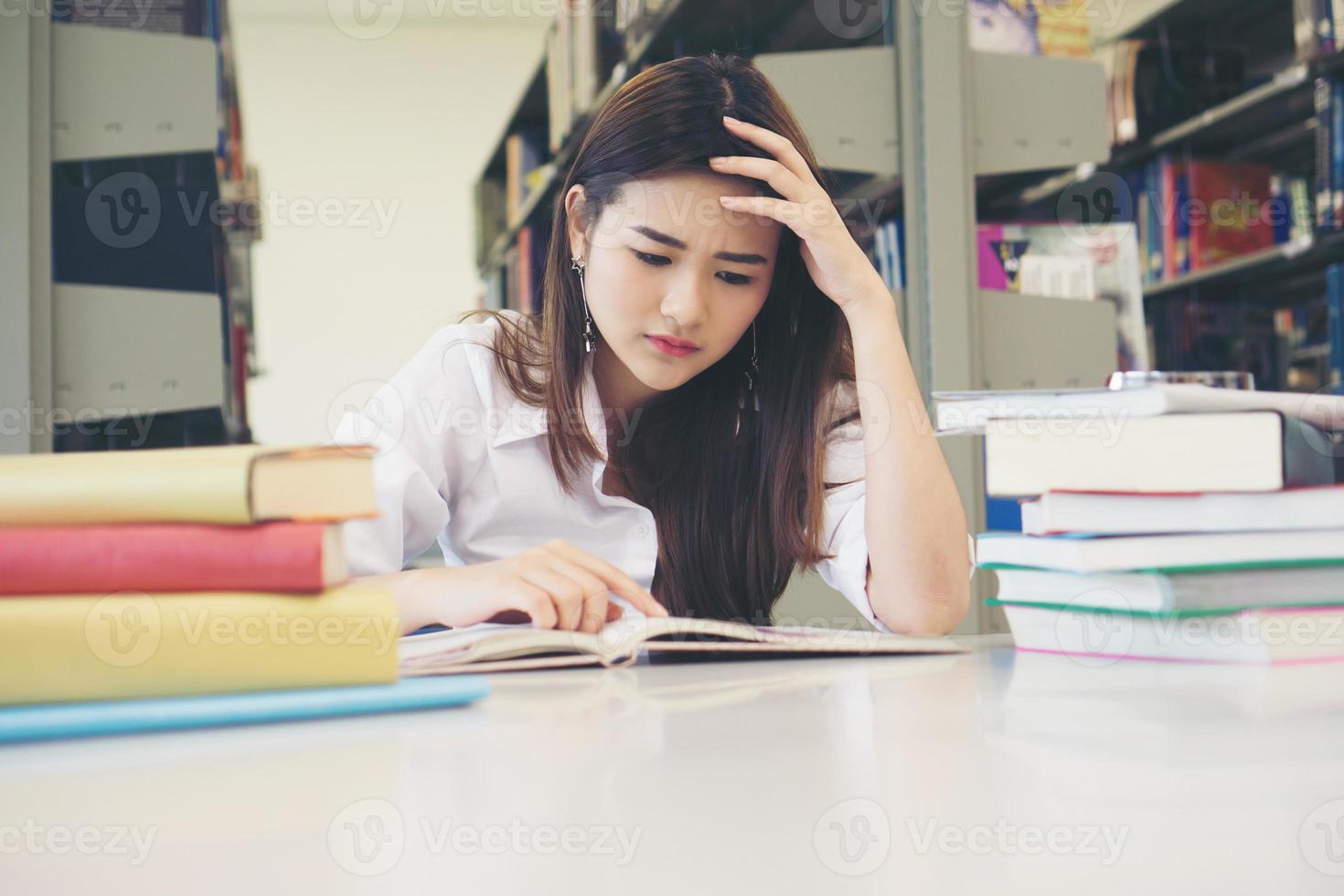 Portrait d'étudiant touchant la tête en lisant un livre dans la bibliothèque du collège photo