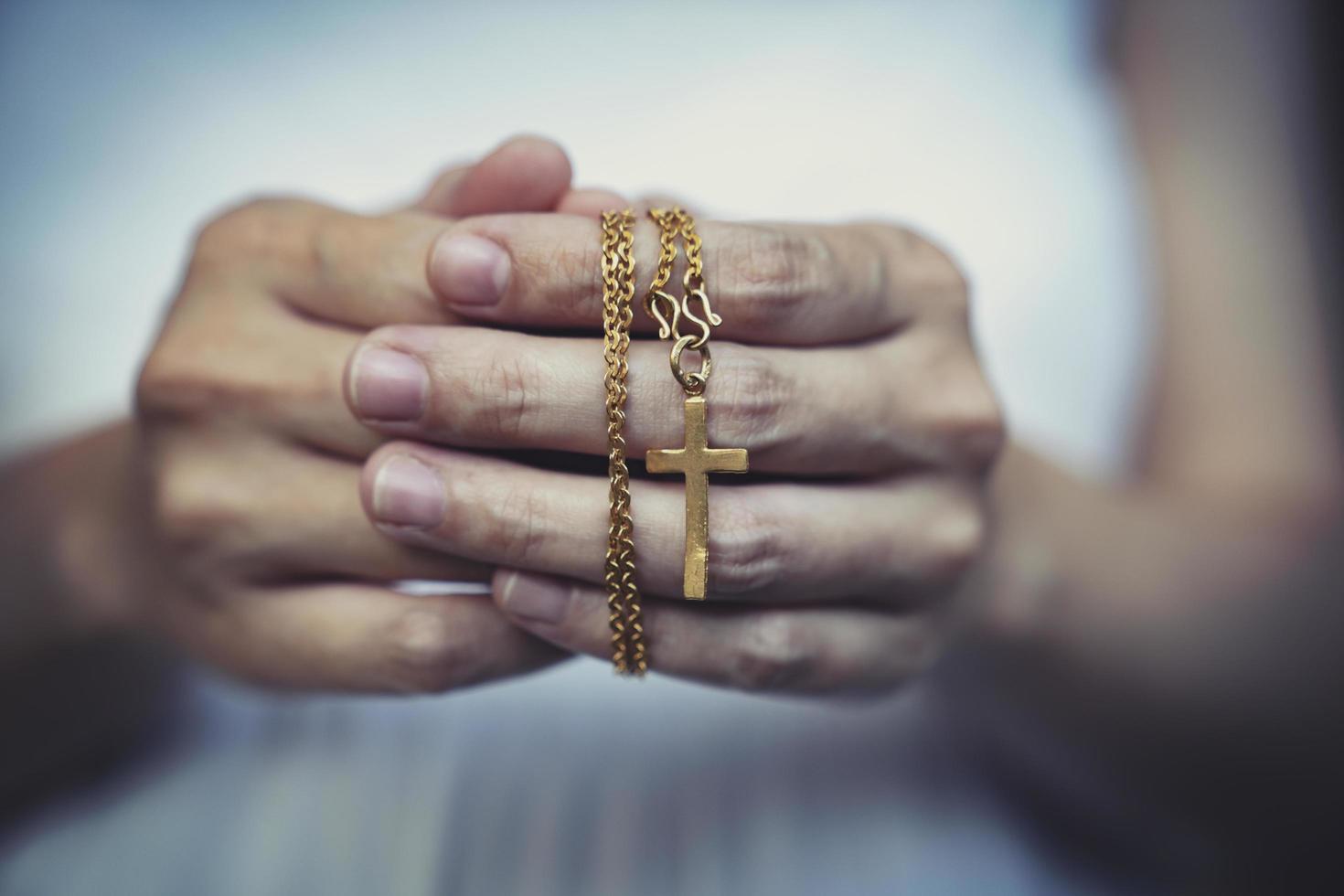 femme mains prier en portant une perles chapelet avec Jésus Christ dans le traverser ou crucifix sur noir Contexte. photo