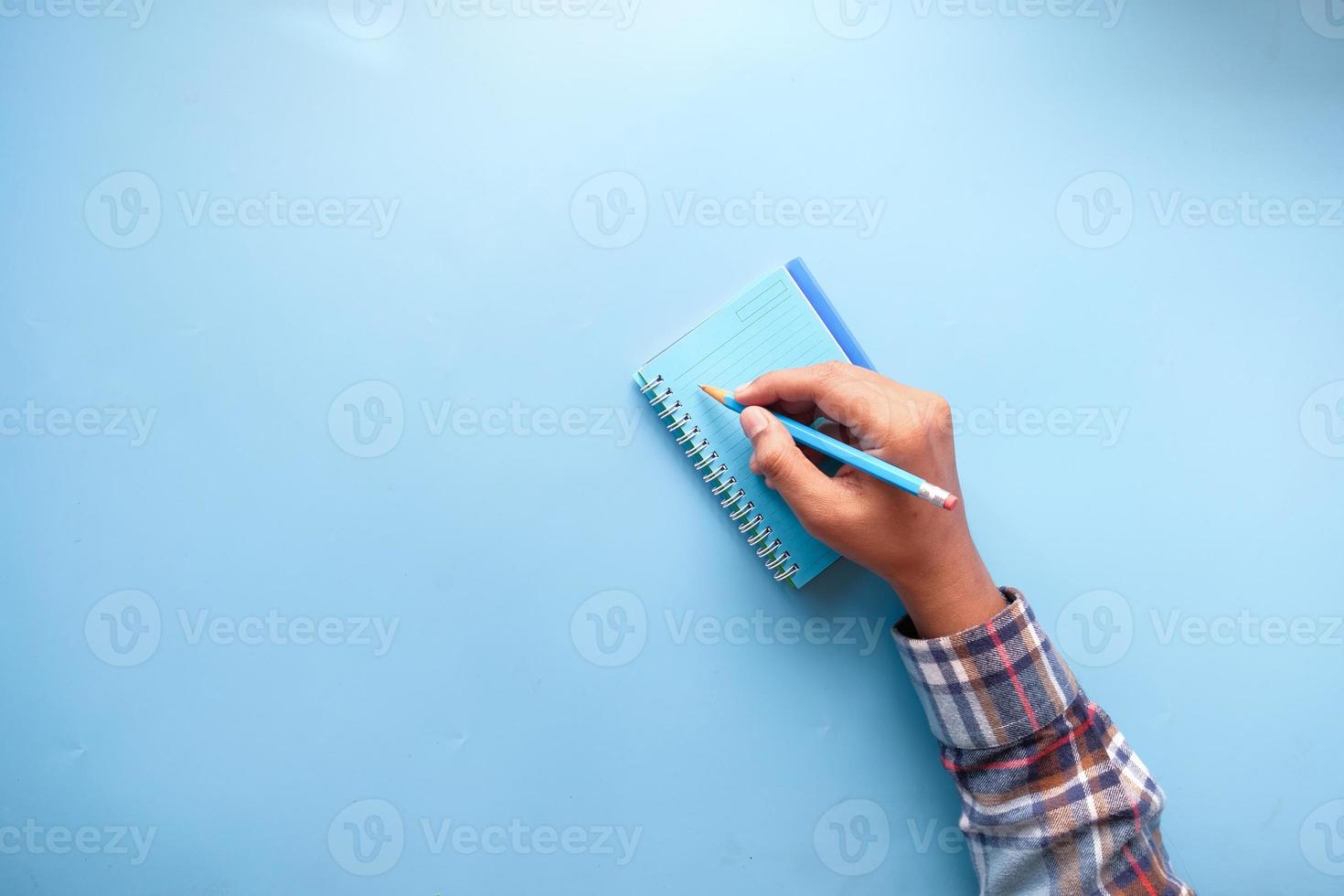 La main de l'homme écrit sur le bloc-notes sur fond bleu photo