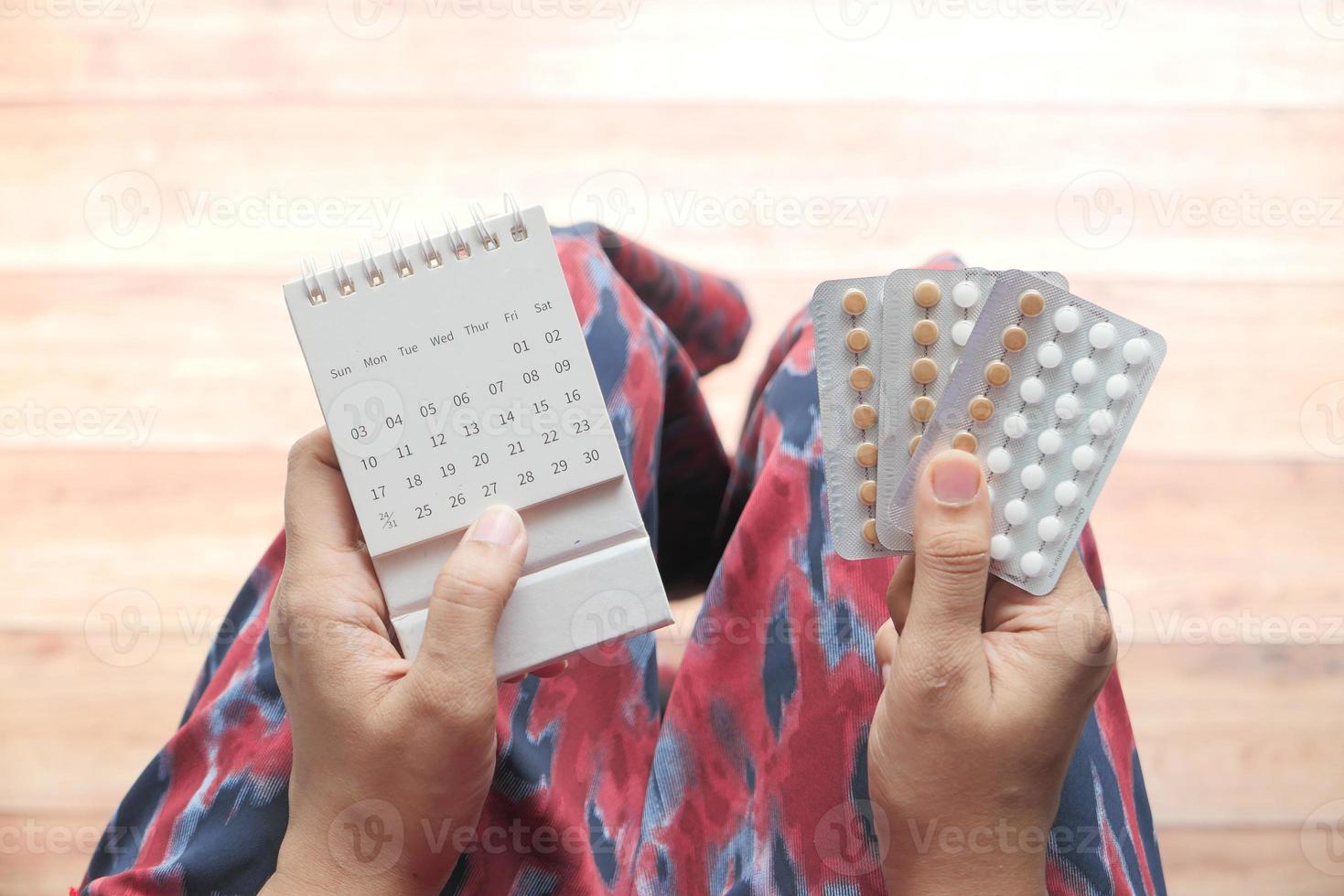 mains de femmes tenant des pilules contraceptives et un calendrier photo