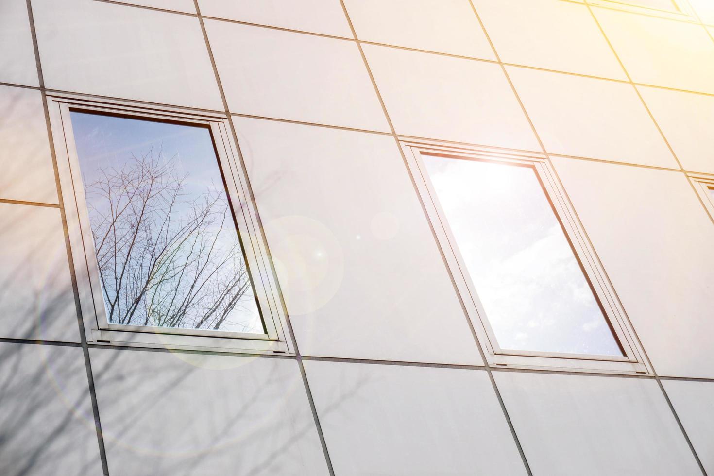 fermer et surgir réflexion et ombre de hiver arbre et brillant bleu ciel sur Bureau bâtiment les fenêtres avec Soleil et lentille éclater. photo