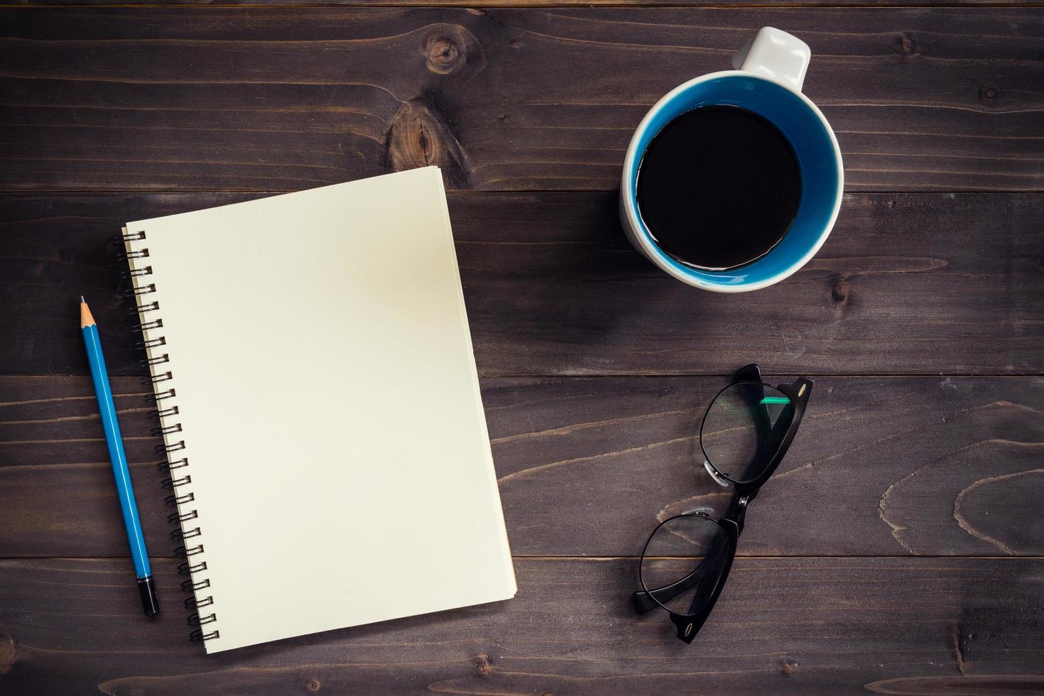 Bureau bois table avec Vide bloc-notes, crayon, des lunettes et tasse de café. photo