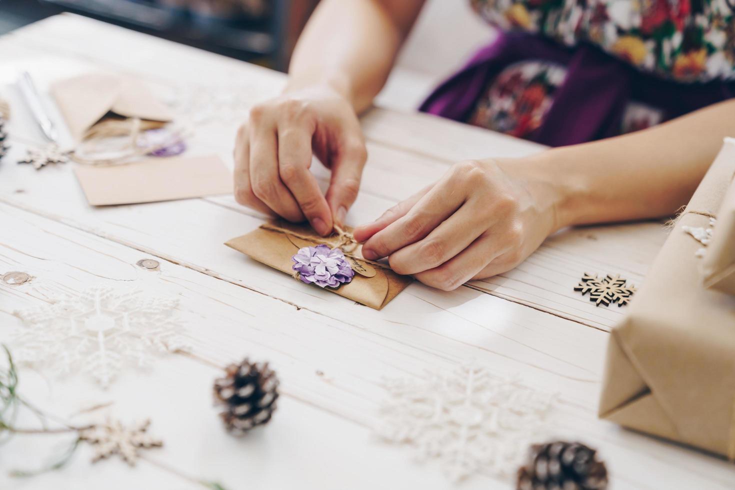 proche en haut de mains en portant emballage cadeau boîte et Noël carte sur en bois table avec Noël décoration. photo