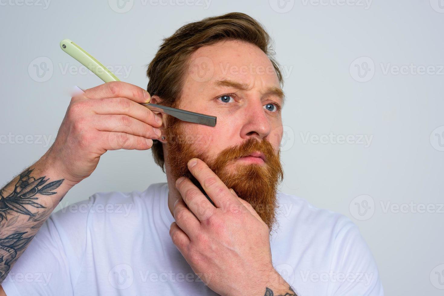 sérieux homme avec lame est concentré sur Coupe le sien barbe photo