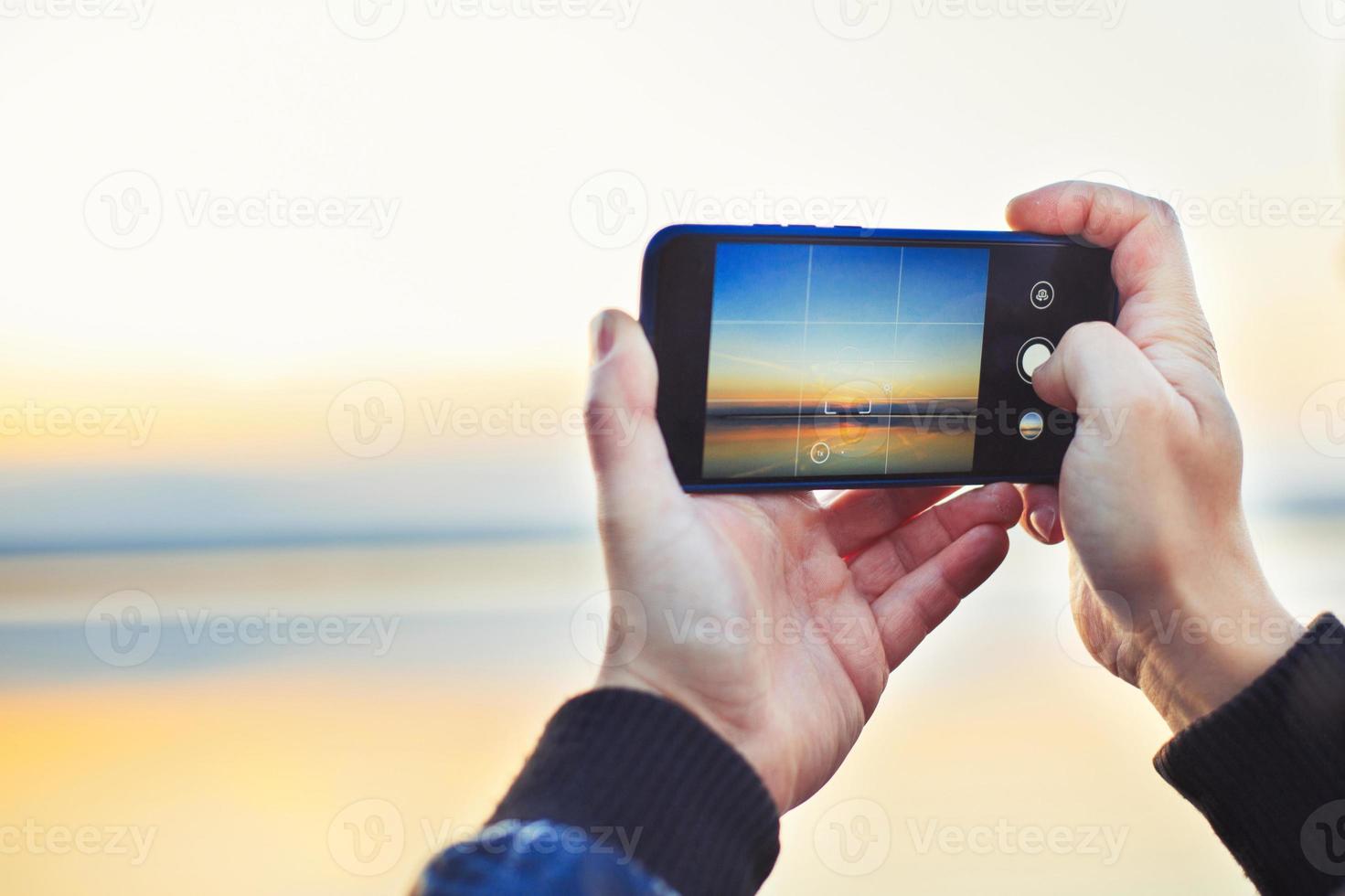 une homme prise une photo de le magnifique le coucher du soleil sur le sien téléphone