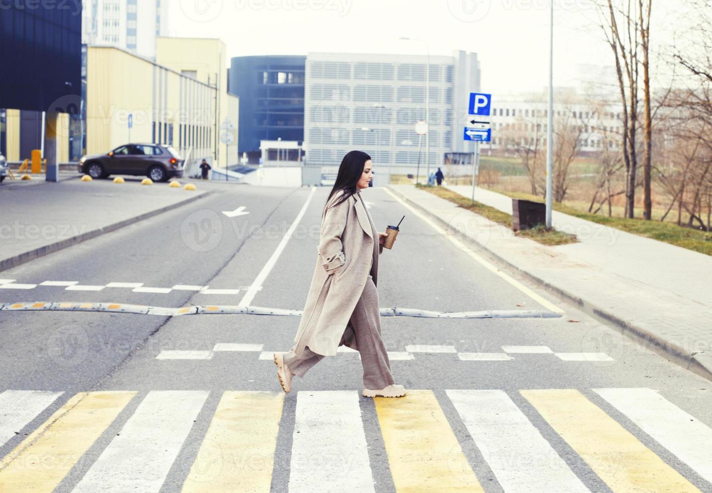 femme en portant café et traversée le route à piéton traversée contre Urbain ville Contexte photo
