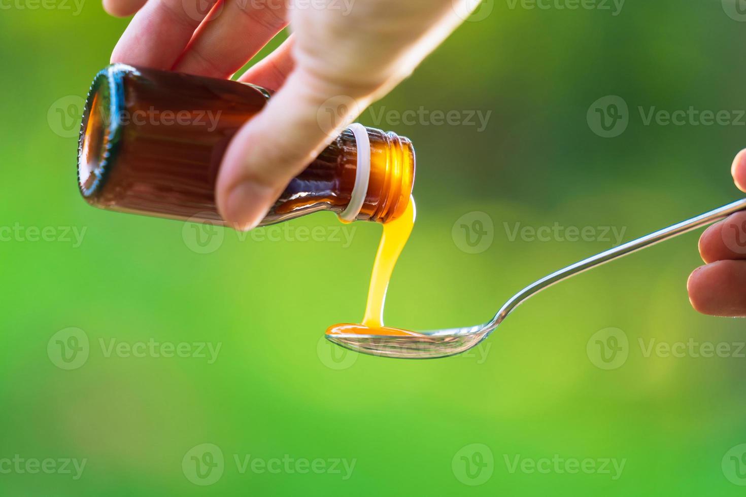 Main de l'homme verser des médicaments ou du sirop antipyrétique de bouteille à cuillère photo