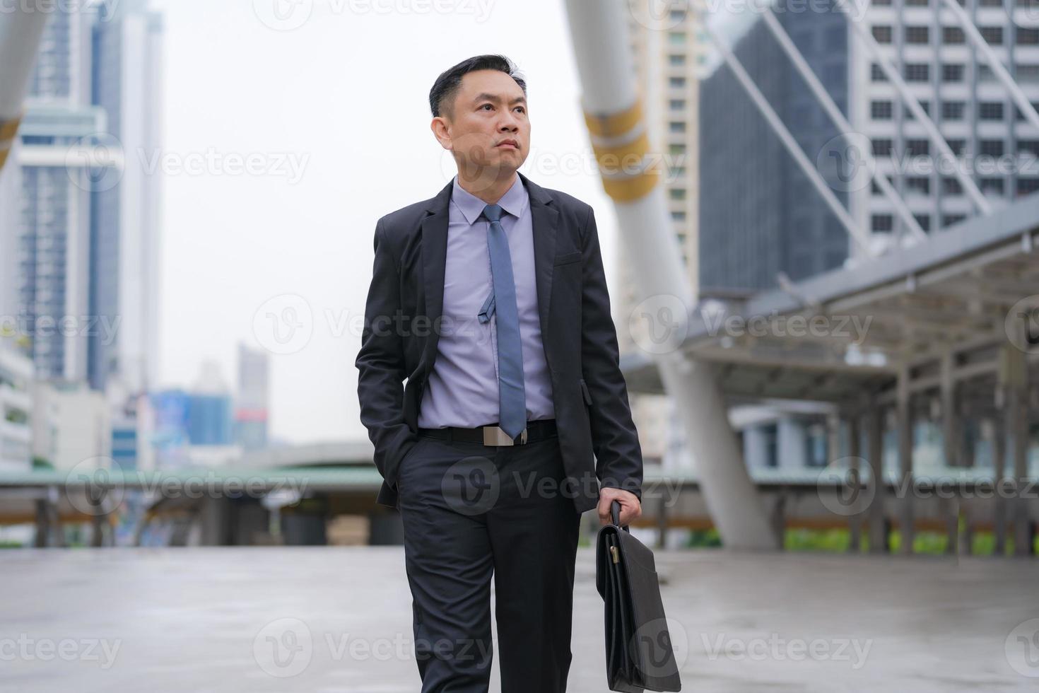 homme d & # 39; affaires asiatique marchant et tenant une mallette avec des immeubles de bureaux dans le fond de la ville photo
