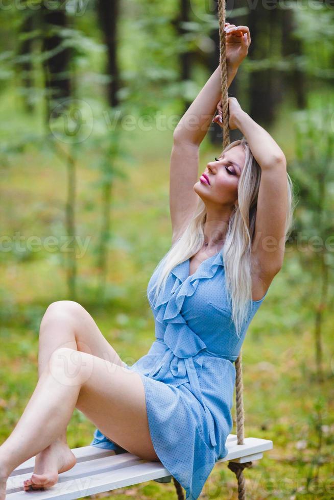 magnifique blond femme dans une bleu robe posant sur une corde balançoire photo