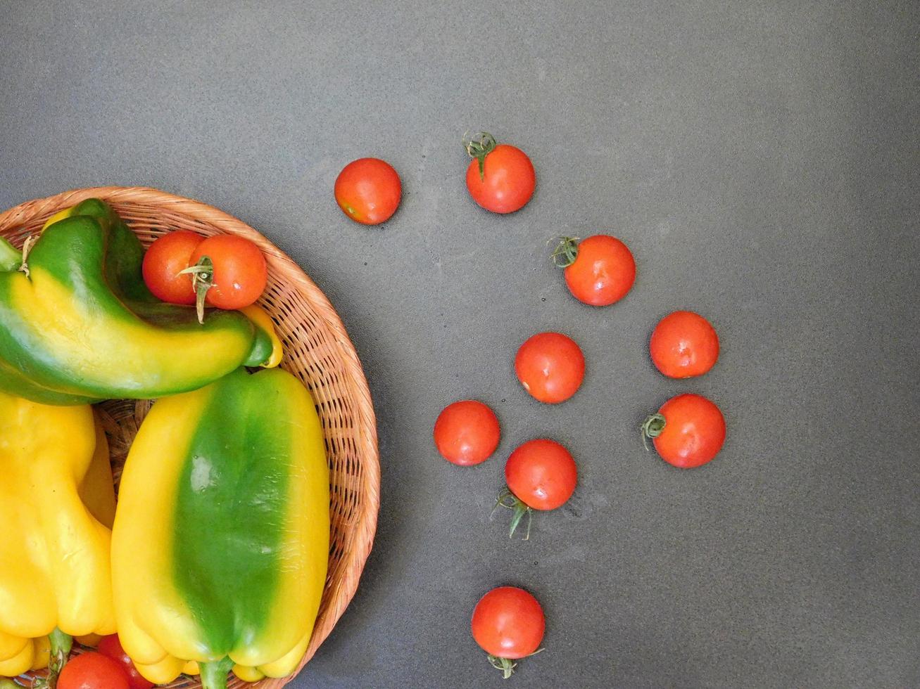 Poivrons et tomates dans un panier en osier sur un fond de table sombre photo