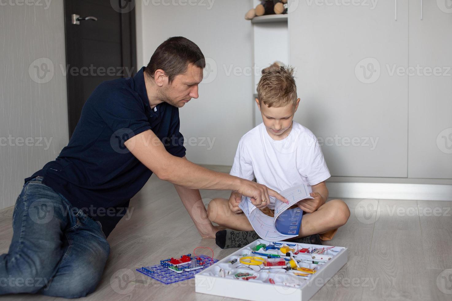 une mignonne garçon dans une blanc T-shirt recueille un électrique designer avec le sien papa dans le pièce photo