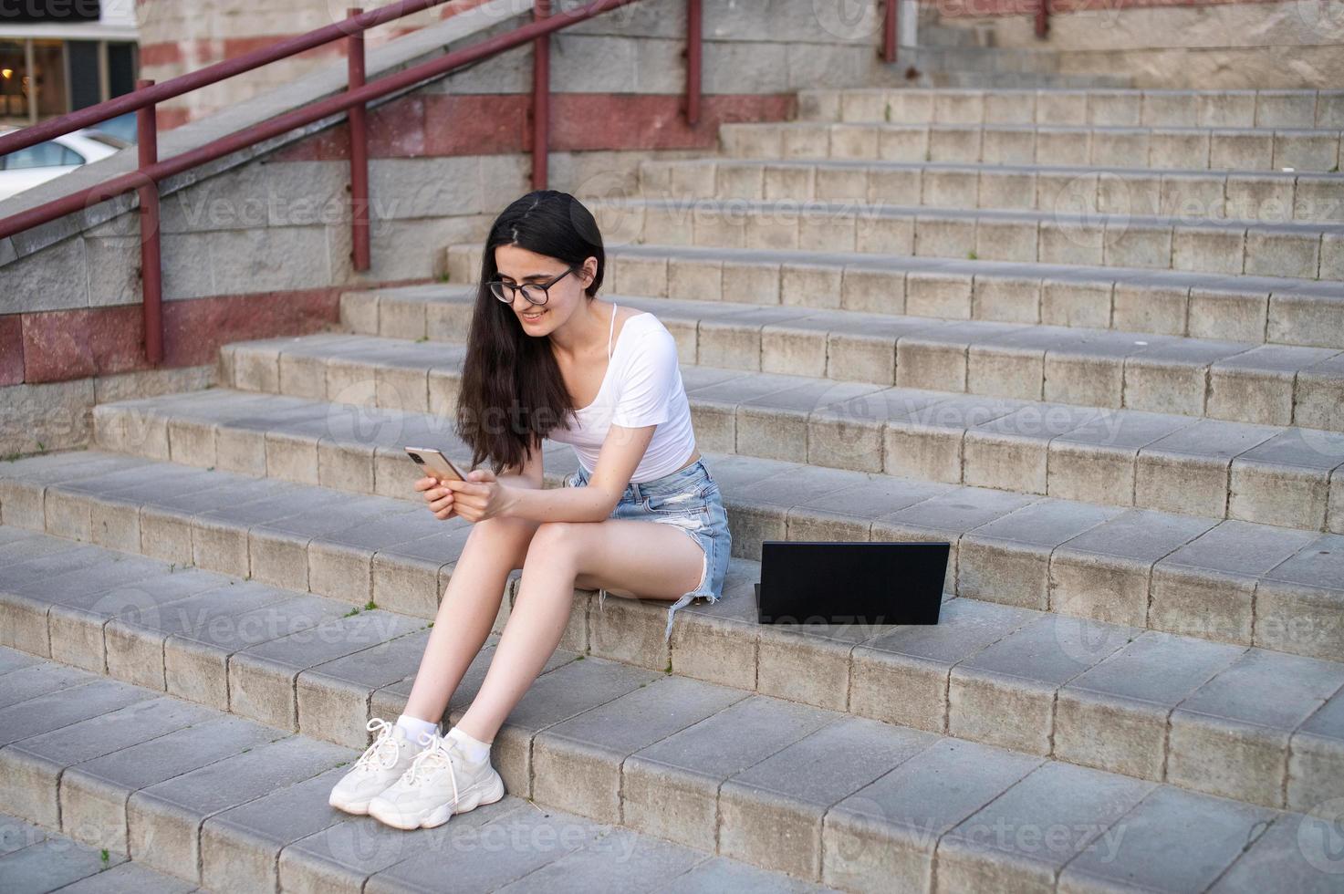 une fille avec des lunettes est séance sur le escaliers avec une portable sur sa tour photo