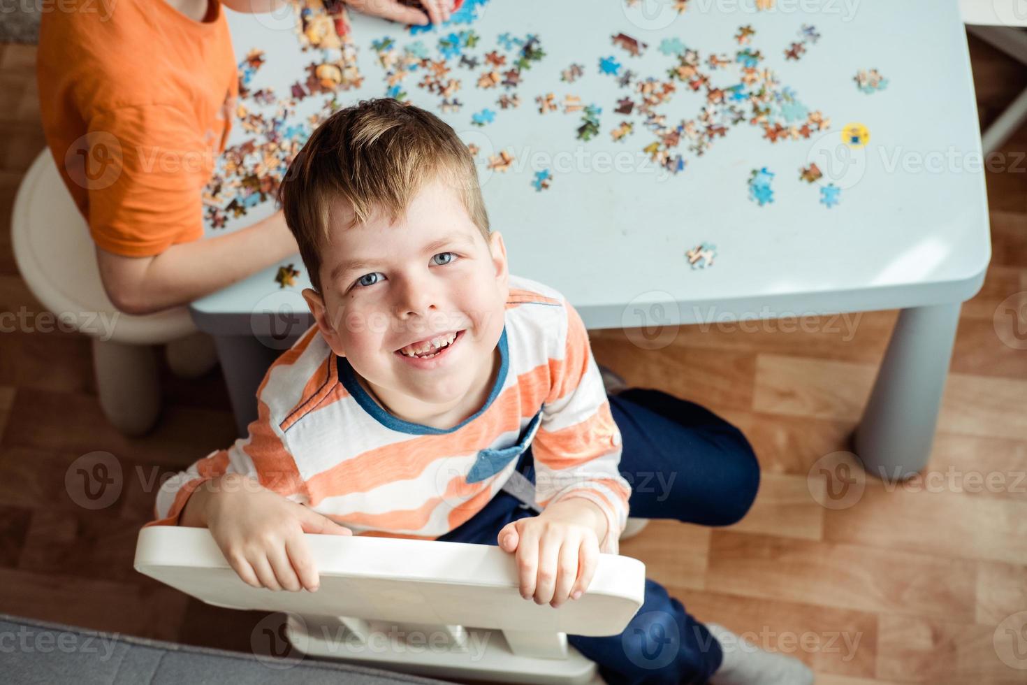 une garçon de 6 ans vieux recueille une puzzle à Accueil et regards à le caméra avec une sourire photo