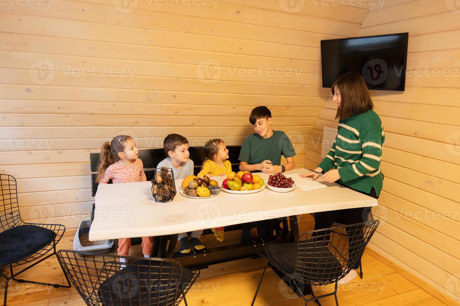 mère avec quatre les enfants manger des fruits dans en bois pays maison sur fin de semaine. photo